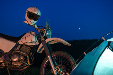 Fototapeta na wymiar Night camping in the mountains forest. tourist have a rest at a campfire near illuminated tent under amazing night sky. Low light. off road motorcycle adventure, enduro.