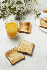 Glass of Fresh Orange Juice, Toast and Branch Spring Flowers on the Light Stone Background. The concept of a Healthy Breakfast