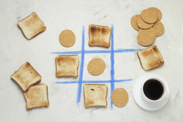 Noughts and Crosses Choice Game Competition  Сookie and Square Toasted Toast, Cup with Black Coffee, White Stone Background Flat lay, top view