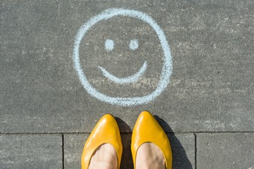 Symbol of happy smiley drawn on the asphalt and woman feet