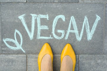Female feet with text vegan written on grey sidewalk