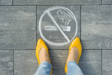 Female feet with picture no smoking painted on the grey sidewalk - obrazy, fototapety, plakaty