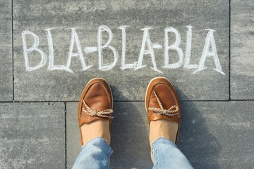 Female feet with text bla-bla-bla written on grey sidewalk