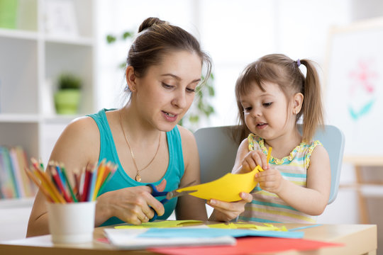 Mother helping her child daughter to cut colored paper