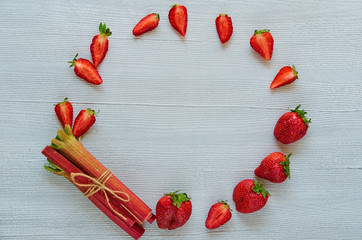 Fresh organic ingredients for baking vegetarian summer pie or healthy dessert - sliced strawberries and raw rhubarb on the gray kitchen table with free copy space on the centre. Top view © oksanafra