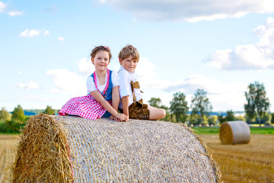 Two kids, boy and girl in traditional Bavarian costumes in wheat field with hay bales