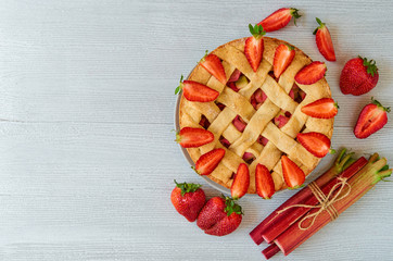 Homemade rhubarb strawberry pie on the gray kitchen background with copy space. Vegetarian summer pie decorated with fresh organic ingredients - sliced strawberries and raw rhubarb. Top view