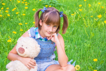 Teenage girl with pigtails and a teddy bear in the hands on a green lawn background with dandelions