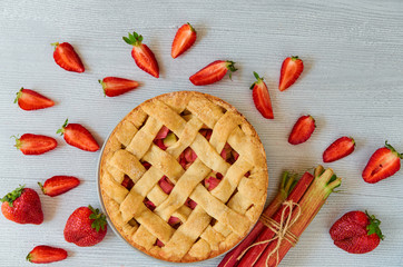 Traditional rhubarb strawberry pie on the gray kitchen table. Vegetarian pie decorated with fresh organic ingredients - sliced strawberries and raw rhubarb. Delicious healthy summer dessert. Top view