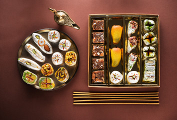 Indian sweets and Mithai in a box and a plate, insense sticks and Aladdin lamp. Diwali festival concept, flat lay, top view