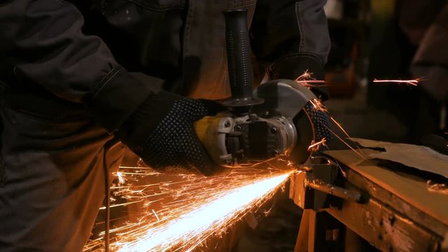 Close up shot - professional blacksmith sawing metal with hand circular saw at forge, workshop. Handmade, craftsmanship and blacksmithing concept