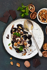 Breakfast from yoghurt with prunes, dates, nuts and chocolate on a concrete green background.