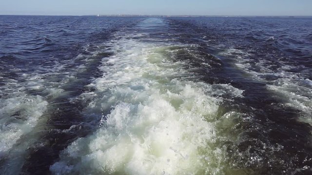 Powerful waves pulled out from fast moving boat, a huge stream of deep blue water with white foam rising up