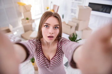 Seizing the moment. Charming young woman taking a selfie in her new apartment while posing for the camera and holding it with two hands