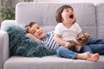 Cute little boy and his crying baby sister on sofa at home