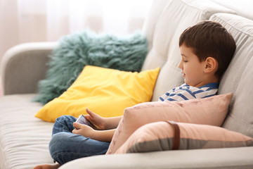 Cute little boy with mobile phone on sofa at home
