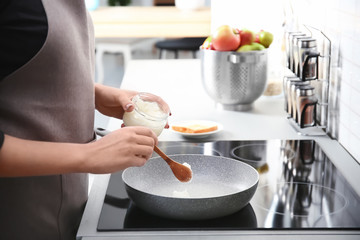 Woman putting coconut oil on frying pan in kitchen, closeup