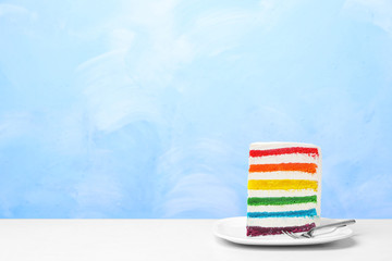 Plate with slice of delicious rainbow cake on table against color background