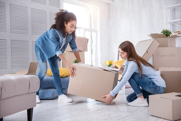 Helping one another. Pretty young girls helping each other and lifting up a heavy box together...