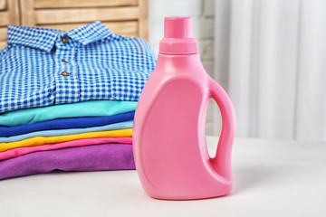 Stack of clean clothes and bottle with detergent on table