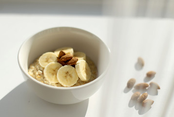 Oat porridge bowl with banana and almonds in a white background
