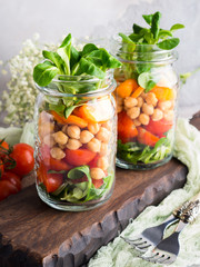 Fresh salad lunch with chickpeas, tomatoes, carrots and valerian served in mason jars