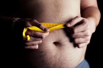 Close-up of a man with excess weight and a big belly against a black background. Measuring tape...