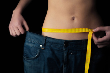 Female stomach on a black background, measuring tape. Proper nutrition, overweight, fitness.