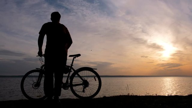 Silhouettes Of Two Cyclists on the coast of sea at sunset time. 