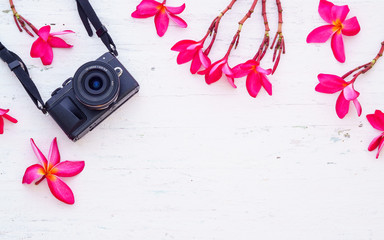 Black camera with pink flora flowers on the grunge white wooden background. Flat lay of travel accessories Background concept.