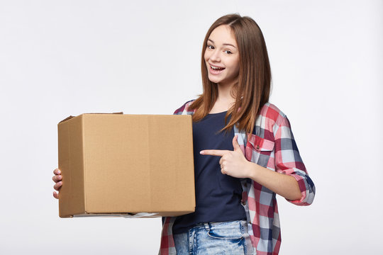 Delivery, relocation and unpacking. Happy young woman holding cardboard box pointing at box with copy space