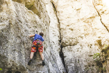 Young girl climber climbs a steep rock at sunset