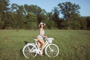 Young woman sits on a white bicycle on a meadow.