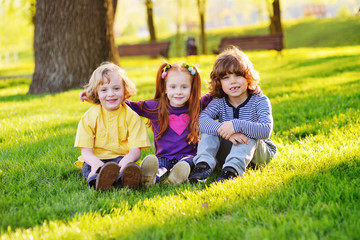 Naklejka na ściany i meble a group of small children in colorful clothes embracing sitting on the grass under a tree in a park laughing and smiling. June 1, Children's Day, vacation, friendship, friends, childhood.
