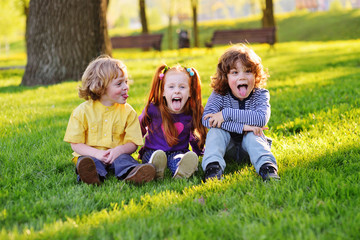 group of happy little children smiling sitting in park on grass under a tree. June 1, Children's Day, friendship, childhood, vacation.