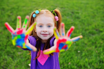Fototapeta na wymiar cheerful little girl with red hair shows her hands dirty with multicolored paints and smiles