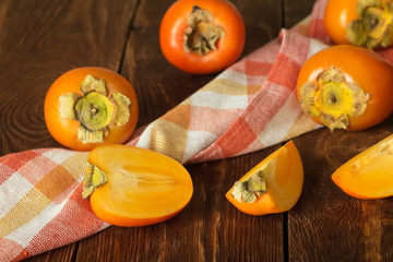 Many whole and cut persimmon fruits with sepals on towel