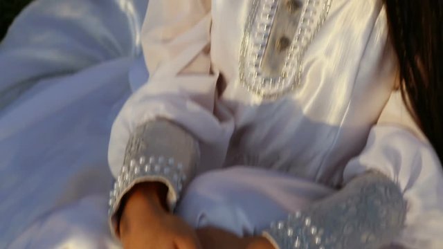 young Asian woman looks at the sky with folded hands. camera with close-up of hands moves to the face. in a beautiful white dress in the light of sunset. spring-autumn