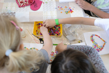 blondes mädchen bastelt am tisch mit knöpfen und kleber