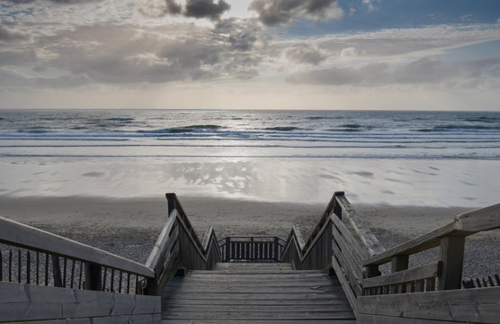 scenic biscarrosse beach in sunset with clouds and wooden footpath stairs, france