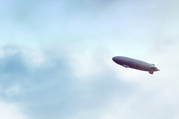 Naklejka na ściany i meble Dirigible flying in cloudy sky, overcast skyscape with airship