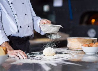 Obraz na płótnie Canvas chef sprinkling flour over fresh pizza dough