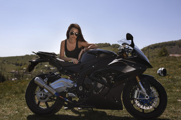 Fototapeta na wymiar Beautiful woman posing with a motorcycle in mountain scenery