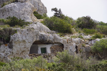 Maison troglodyte en pierre sous un rocher dans la campagne de l'île de Minorque aux Baléares, Espagne.