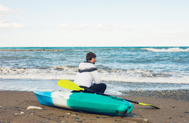 Man carrying his kayak along the shore.