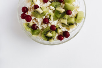 Delicious cottage cheese with kiwi pieces and cranberries in bowl on white background, closeup, healthy breakfast