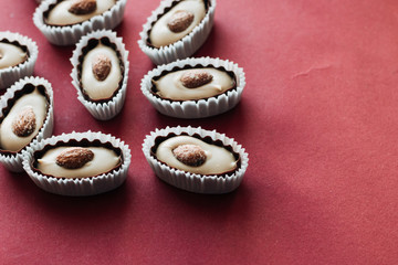Flat lay of delicious praline sweets with almonds on red background