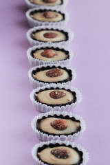 Row of delicious praline sweets with almonds on purple background