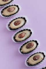 Row of delicious praline sweets with almonds on purple background