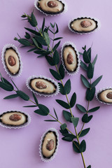 Flat lay of delicious praline sweets with almonds on purple background with green spring twig